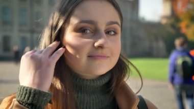 Uzun siyah varisi ve kahverengi gözleri ile gorgeoud beyaz kızın yakın çekim yüz kameraya sakince gülümseyerek bakıyor ve düzeltiyor saç, kentsel arka plan, meleklerim