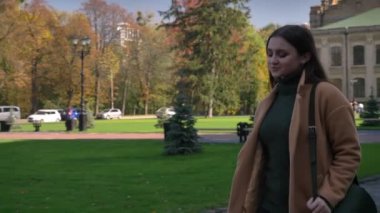 Korku veren beyaz gülümseyen kadın hareket ediyor ve park yakınındaki karşıya ve telefonunu kullanarak rahat hareket, kentsel tarzı, güneşli bir gün