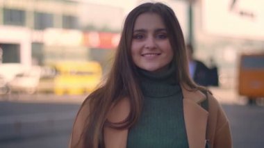 Harika beyaz kadın yan yol ayakta ve kamera, şehir alanında, rahatlatıcı rahat tarzı düz mutlu yüz ile bakıyor