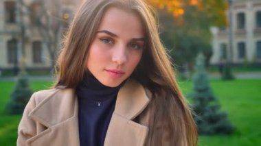 Sevimli beyaz kadın sakin bir şekilde duran ve kamera sakin ve kentsel sunlights açık arka planda utangaç bakarak