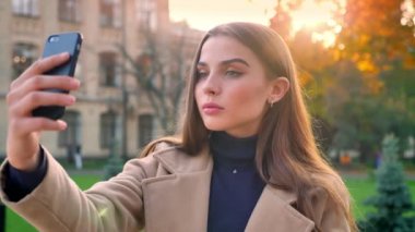 Eğlenceli mutlu beyaz kız selfies telefonuyla ilgili alarak ve gündüz kentsel güzel arka plan üzerinde izole dururken komik surat
