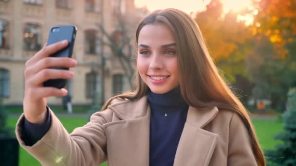 华丽的高加索女孩拿着她的手机, 并采取自己的照片, 而独自站着, 显示快乐的情绪, 城市插图 — 图库视频影像