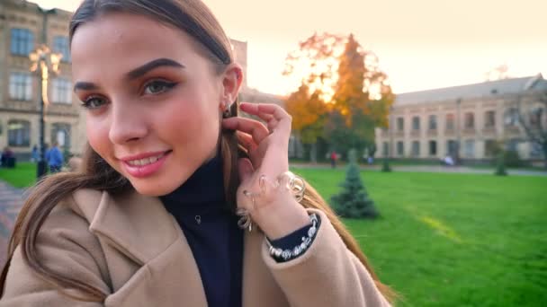 Přírodní čistá krásná Kavkazský žena drží kameru a umělecké grimas stoje venkovní, spokojeně uvolněná, na pozadí města sunshines venkovní — Stock video