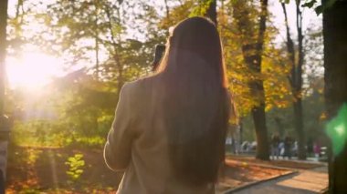 Beyaz esmer kız muhteşem görüntüleri güneş parlar yüzünde ayakta ve seyir muhteşem doğa açık, park illüstrasyon, sonbahar, holding telefon