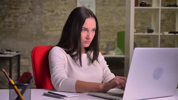 Женщина работает в офисе перед ноутбуком и делает заметки в своем блокноте — стоковое видео
