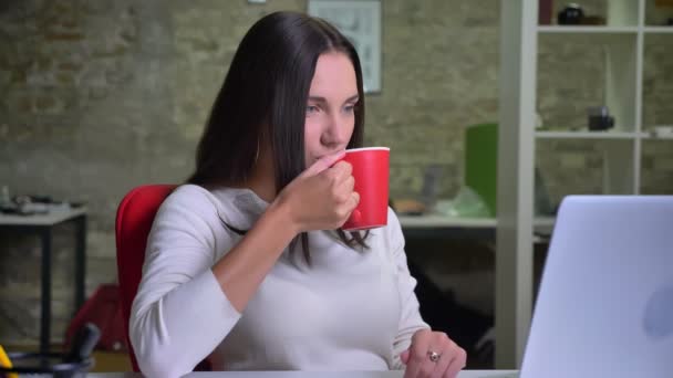 노트북, 앞 사무실에서 일 하는 여자는 카메라를 돌아서 멋지게 윙크 — 비디오