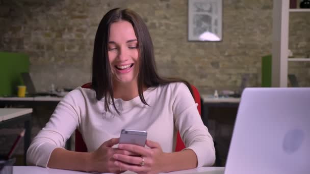 Mulher surfando o smartphone fica muito alegre e explode rindo no escritório — Vídeo de Stock