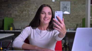 İş kadını ofiste onun smartphone kullanarak ve gülümseyen görüntülü sohbet konuşuyor.