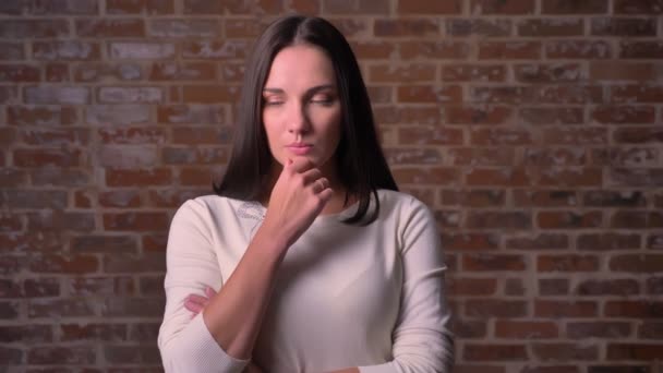 Vrouw horloges zorgvuldig naar de camera met haar arm in de buurt van de kin op de achtergrond van een bricken — Stockvideo