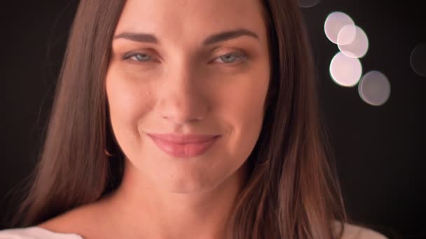 Frau lächelt demütig in die Kamera vor blauem Hintergrund — Stockvideo