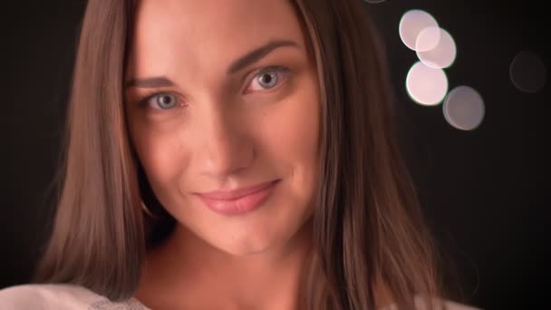 若い女性は彼女の眉毛を持ち上げる、blured ライトの背景にカメラでいちゃつく彼女の唇をかむ — ストック動画