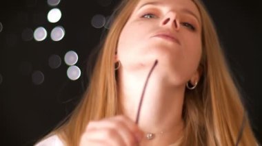 Harika sarışın beyaz kadın üzerine onun gözlük koyuyor ve güvenle kamera karanlık studio, tek başına dururken düz bakarak çekim ışık