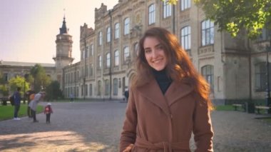 Seyir ve neşeyle kamera sakin ve mutlu yüz, sonbaharda eski binalar üzerinde duran gülümseyen sevimli beyaz kadın hareket, çekim