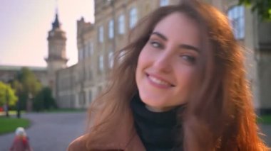 Muhteşem bir esmer beyaz kadın sıcak güneşli bir günde kamera ve shillind eski binalar yakın kentsel alanda yakın arıyor