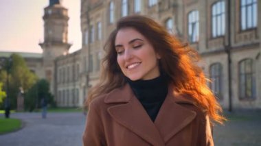 Güzel gülümseyen beyaz kız üzerinde kentsel binalar sunlights içinde tek başına duran ve mutlu bir şekilde açık havada asılı