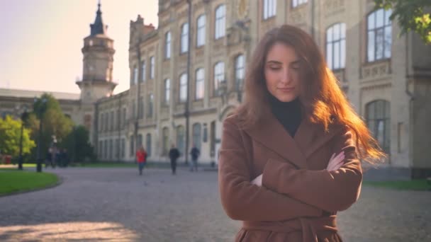 Incroyable fille brune caucasienne est debout à l'extérieur droite et regardant la caméra avec position naturelle détendue, bâtiments sur le fond — Video