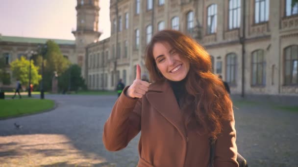 Awesome Kaukasische vrouw is permanent ontspannen in sunlights en tonen zoals teken bij camera in zonnige herfstdag op stad gebouwen achtergrond — Stockvideo