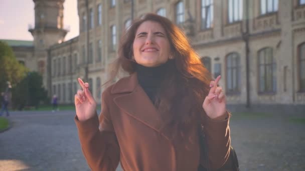 Uśmiechnięte dziewczyny Brunetka kaukaski w Pterry stoi i życząc powodzenia pokazując palce skrzyżowane gest o aparat, słoneczny dzień, ilustracja miejski — Wideo stockowe