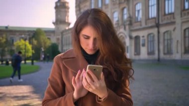 Mutlu beyaz esmer kadın telefonunu kullanarak, bir elinde tutan ve kentsel alanda duran ve güzel gülümseme gösterilen selfies alarak