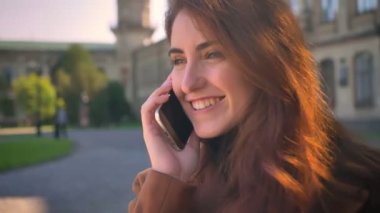 Beyaz kadın konuşurken Closeup etrafında dönen ve konuşmaya büyük gülümseme ve kentsel arka plan üzerinde sakince ayakta sanatsal duyguları ile rahat.