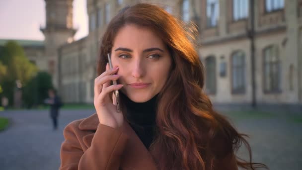 Filmato di bel viso di donna caucasica che ha una conversazione telefonica, parlando astuto stadning straignt vicino alla fotocamera, illustrazione urbana — Video Stock