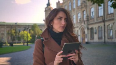 Sevimli beyaz esmer kız bakmak ve onun aygıt, kentsel illüstrasyon, modern kişi gençler içinde kullanarak el ile rahat ve tutan tablet duruyor