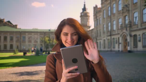 Doux cacasien heureux brunette femelle regarde tablette et agitant à la caméra web tout en se tenant à l'extérieur, parler et se détendre pendant la journée chaude ensoleillée dans la zone urbaine — Video