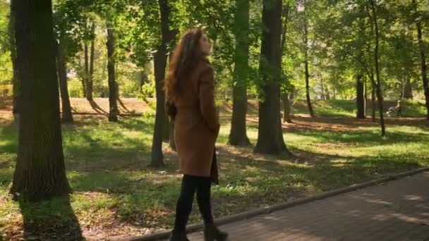 Caminar mujer caucásica con una bonita sonrisa está avanzando en un hermoso parque y mirando a los árboles verdes con felicidad, ilustración al aire libre — Vídeo de stock