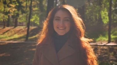 Çok güzel beyaz esmer gençler içinde ayakta ve kamera chill ağaçlar ve arka plan üzerinde park yakınında yüzünde mutlu gülümseme ile seyir.