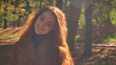 Muhteşem beyaz esmer kadın güneş ışığı altında duran ve neşeyle açık havada güzel park, mutluluk resimde gülümseyen