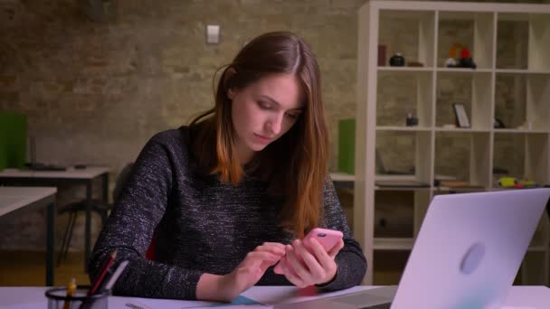 Jeune femme rousse caucasienne surfer sur le smartphone et change les émotions de la joie à la perplexité au bureau . — Video