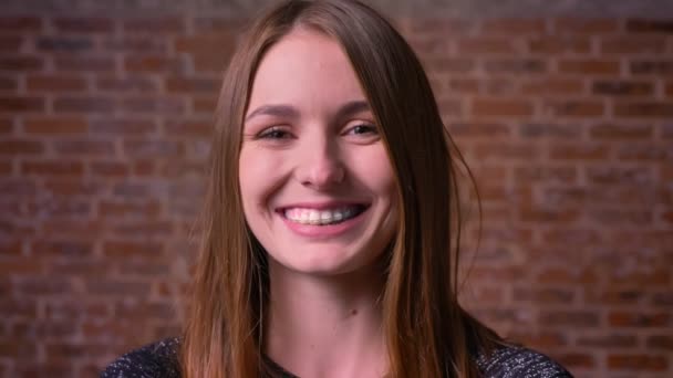 Retrato de close-up da jovem mulher de gengibre com olhos felizes sorrindo deliciosamente para a câmera no fundo de tijolos . — Vídeo de Stock