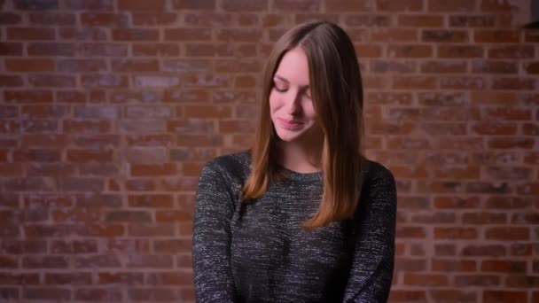 Portrait of shy redheaded girl on bricken background, screwing up her eyes and laughing — Stock Video