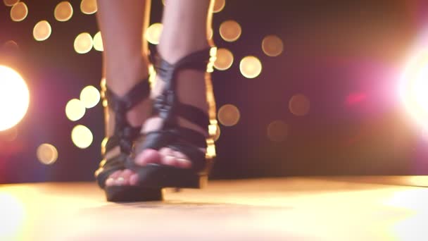 Великолепные ноги на высоких черных стильных каблуках в движении к камере, стоя, меняя положение, на ярком фоне — стоковое видео