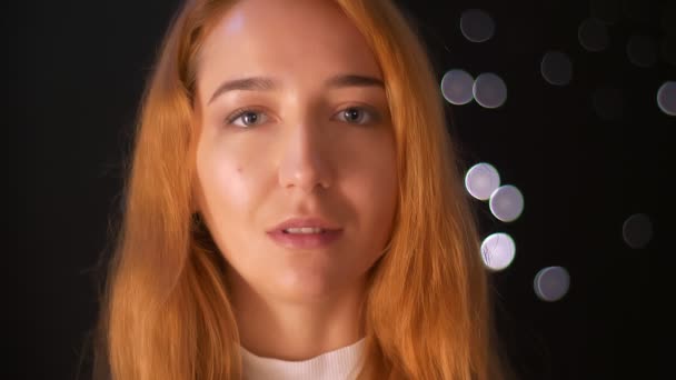 Close-up portrait of beautiful ginger woman standing isolated on black background and looking calmly at camera, indoors — Stock Video