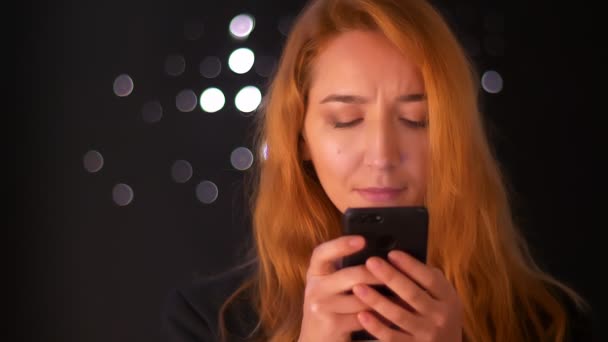 Menina gengibre caucasiano bonito está segurando seu telefone e olhando para a tela concentrada com rosto bonito focado, ilustração artística, fundo preto — Vídeo de Stock