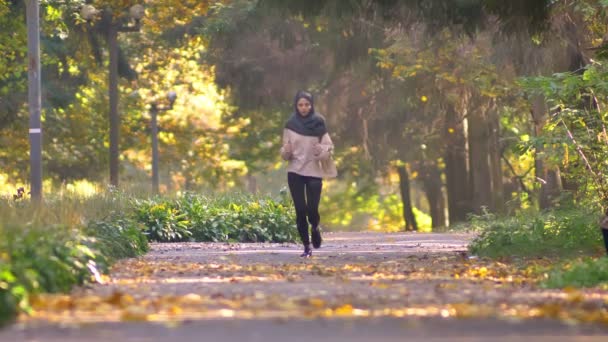 Мусульманка в хиджабе бегает трусцой в осеннем парке — стоковое видео