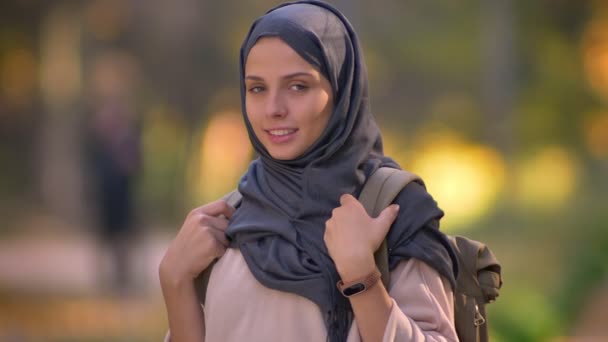 Close-up retrato de menina muçulmana no hijab olhando para a câmera com sorriso, mostrando a mochila . — Vídeo de Stock