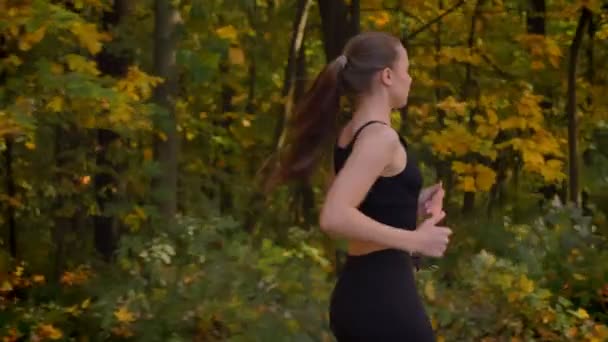 Dolly shot di giovane ragazza magra in tuta che va a correre nel parco autunnale . — Video Stock