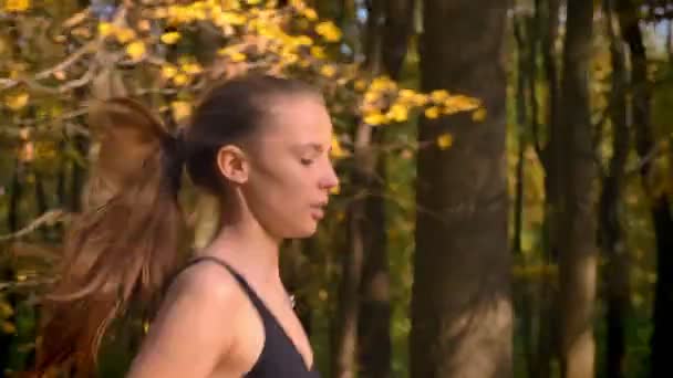 Dolly shot, portrait en gros plan de profil de jeune fille mince en combinaison qui va faire du jogging dans le parc automnal . — Video