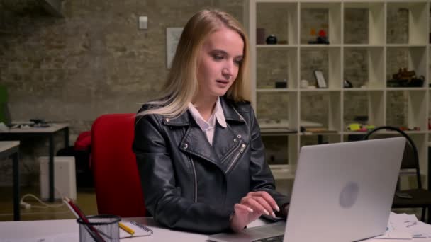 Artistic blonde worker is looking at screen on computer while sitting and happy laughing after noticing funny thing in screen, sitting at desktop , office background — Stock Video