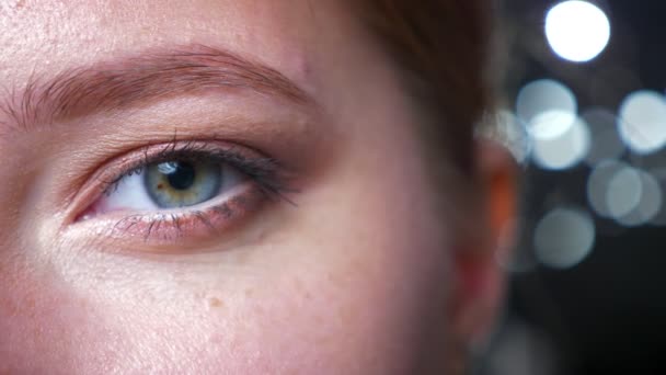 Aufnahmen von Nahaufnahme-Lidschatten auf grünem fokussiertem Auge einer schönen kaukasischen Frau, die mit freundlichem Blick und dunklem Hintergrund direkt in die Kamera blickt — Stockvideo