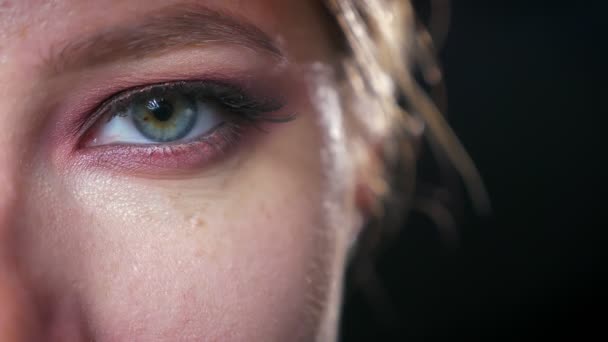 Gros plan oeil bleu et vert avec des fards à paupières colorés impressionnants de fille caucasienne, regardant refroidir la caméra, fond sombre — Video