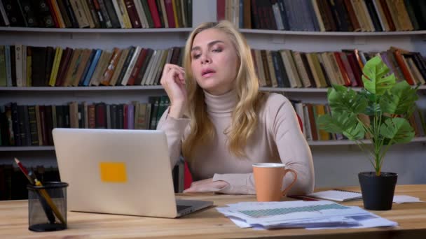 Porträtt av blonda medelålders kaukasisk kvinna arbetar på kontor med laptop och tänker på bokhyllor bakgrund. — Stockvideo