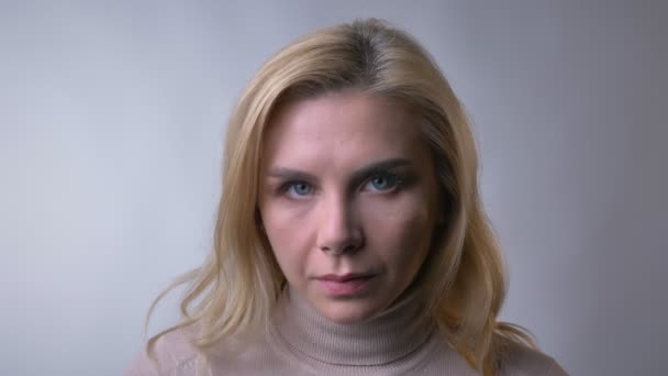 Close-up portret Pani blondynka w średnim wieku oglądanie poważnie do aparatu na szarym tle. — Wideo stockowe