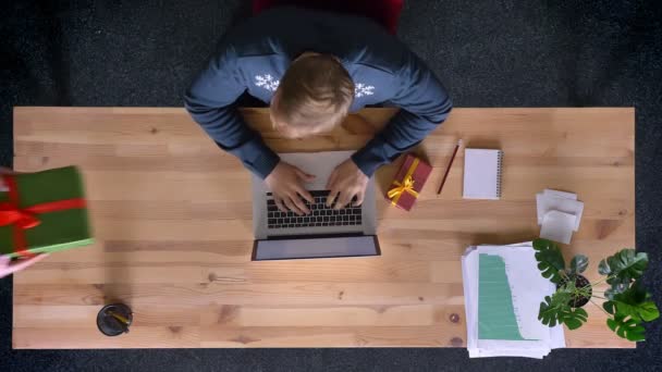 Vista de arriba hacia abajo del hombre que trabaja en la oficina delante de la computadora portátil intercambiando regalos con su colega sin abrirlo . — Vídeo de stock