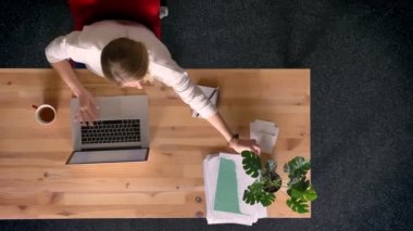 Dolly atış yukarıdan aşağıya istatistik raporları laptop önünde Office ile çalışan raslantı giyimli kadın görünümünü