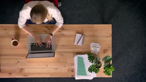 Dolly tiro de cima para baixo vista de mulher casualmente vestida trabalhando e fazendo anotações no escritório na frente do laptop . — Vídeo de Stock