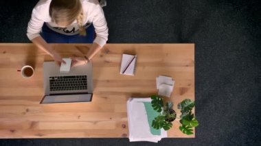 Dolly atış yukarıdan aşağıya ile smartphone laptop önünde ofiste çalışan raslantı giyimli kadın görünümünü.