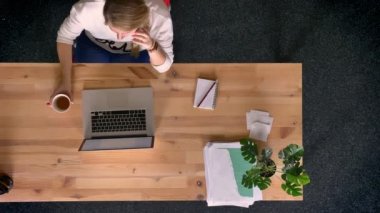 Dolly atış yukarıdan aşağıya telefonda konuşuyor ve laptop önünde ofisindeki kahve içme raslantı giyimli kadın görünümünü.